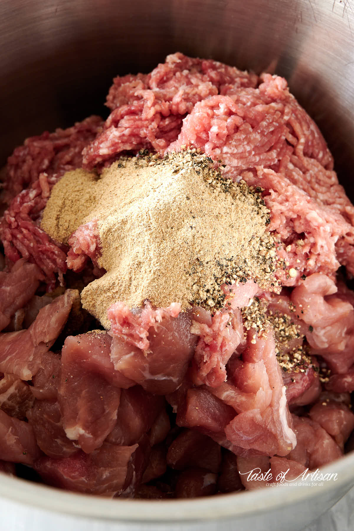 Meat for kielbasa in a bowl with white and black pepper on top.