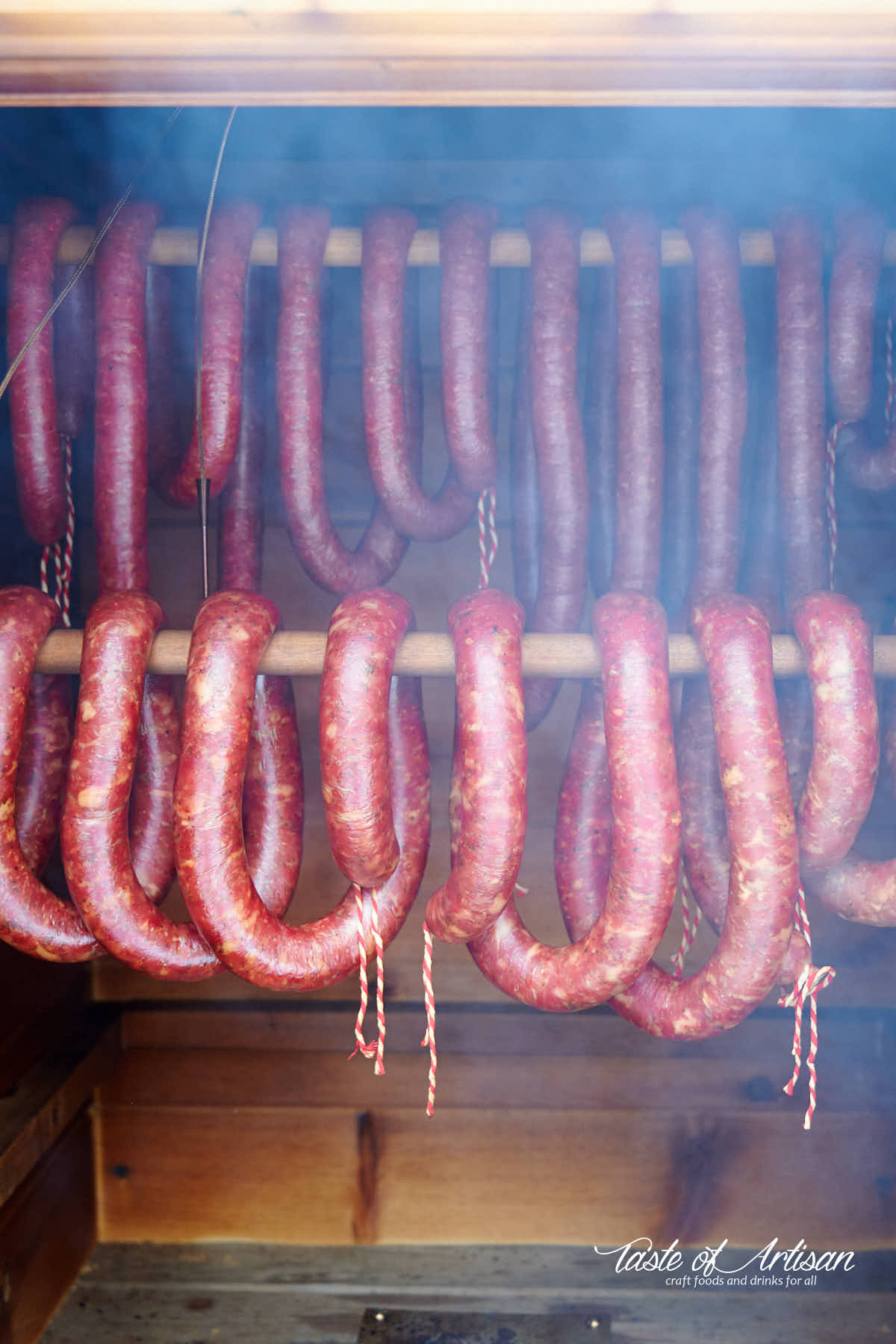 Coils of sausage smoking in a smokehouse, smoke coming out the door.