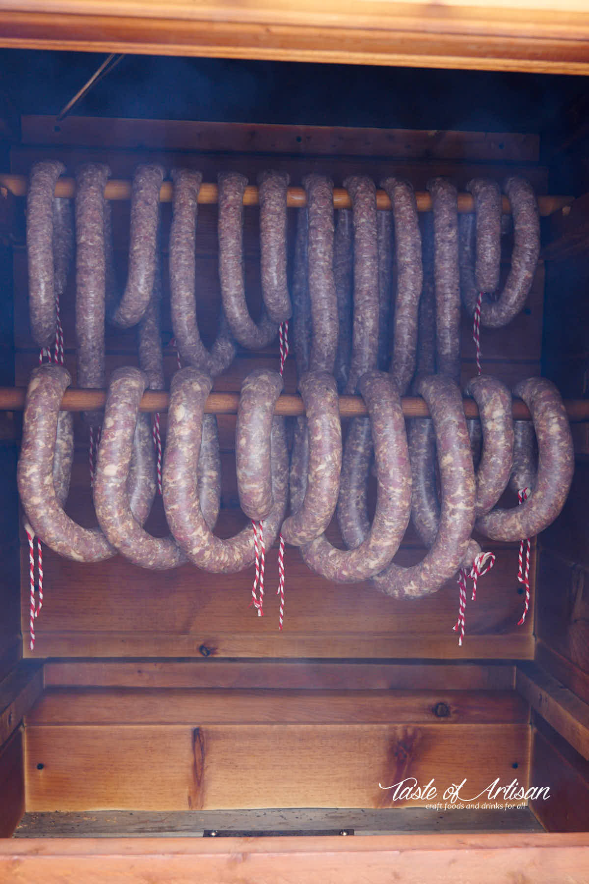 Raw sausages handing on sticks in a smokehouse.