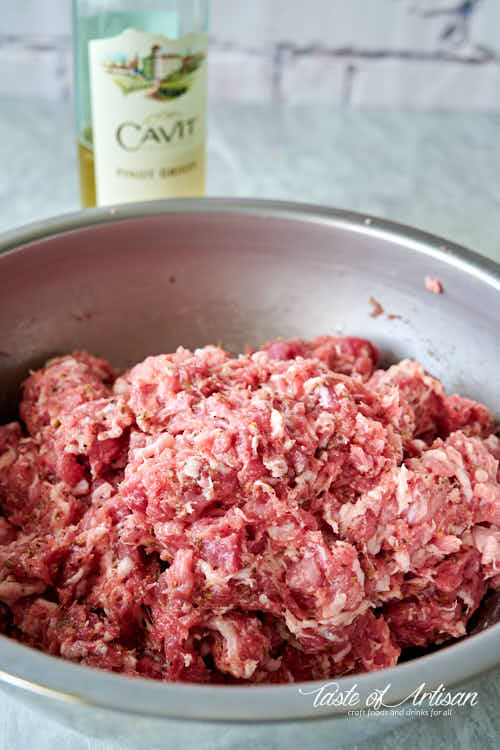 Ground meat in a bowl, with a bottle of wine on the background.