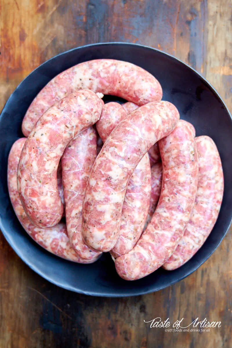 Freshly made Italian sausage links on a black plate.