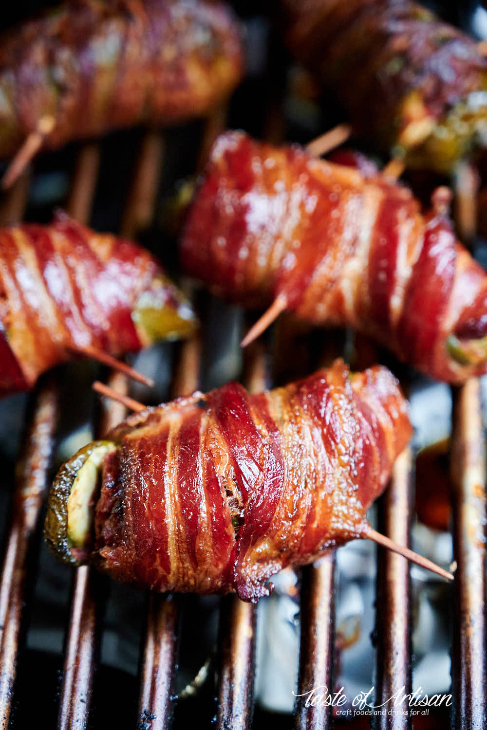 Bacon wrapped jalapeno peppers stuffed with brisket on a grate of a smoker.