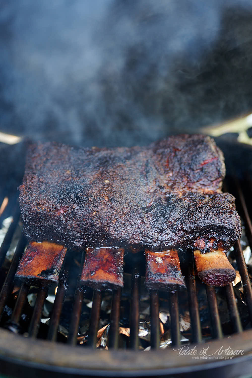 Beef short ribs on a smoker, smoke coming out.
