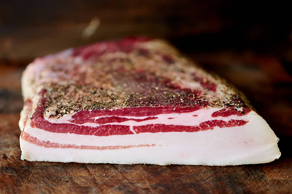 A slab of home cured bacon a cutting board.