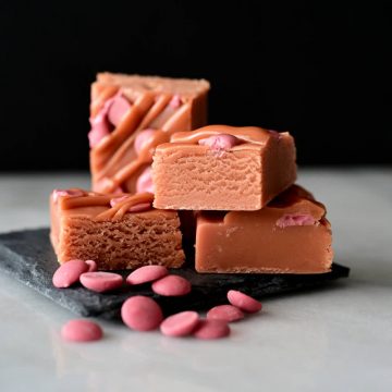 Pieces of chocolate fudge with pink chocolate chips next by, on a black stone board.