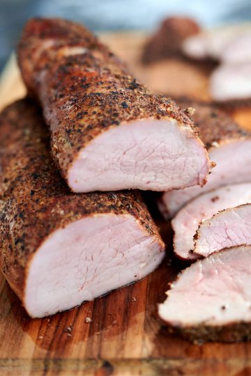 Sliced smoked pork tenderloin on a cutting board, juicy and moist.