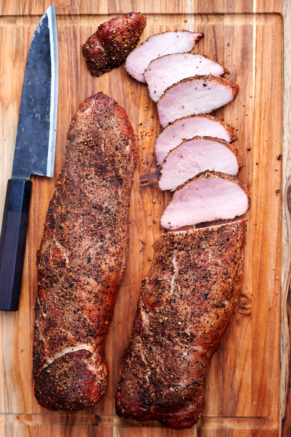 Top down view of two pork tenderloins, one partially sliced, on a board.