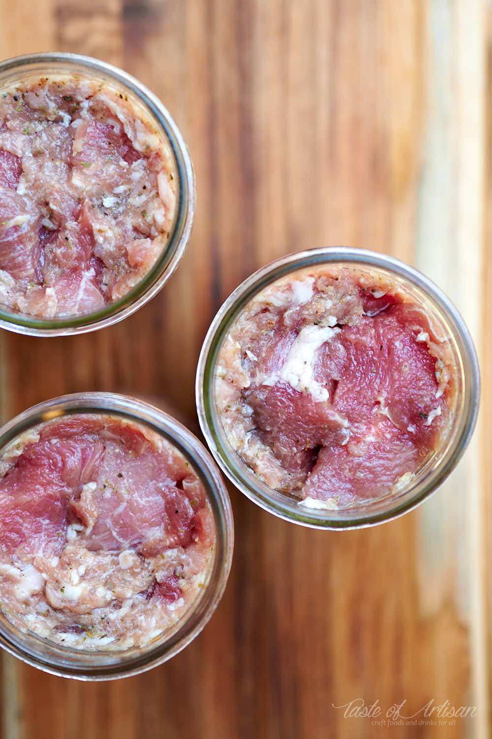 Stuffing pork chunks and ground pork in glass jars.
