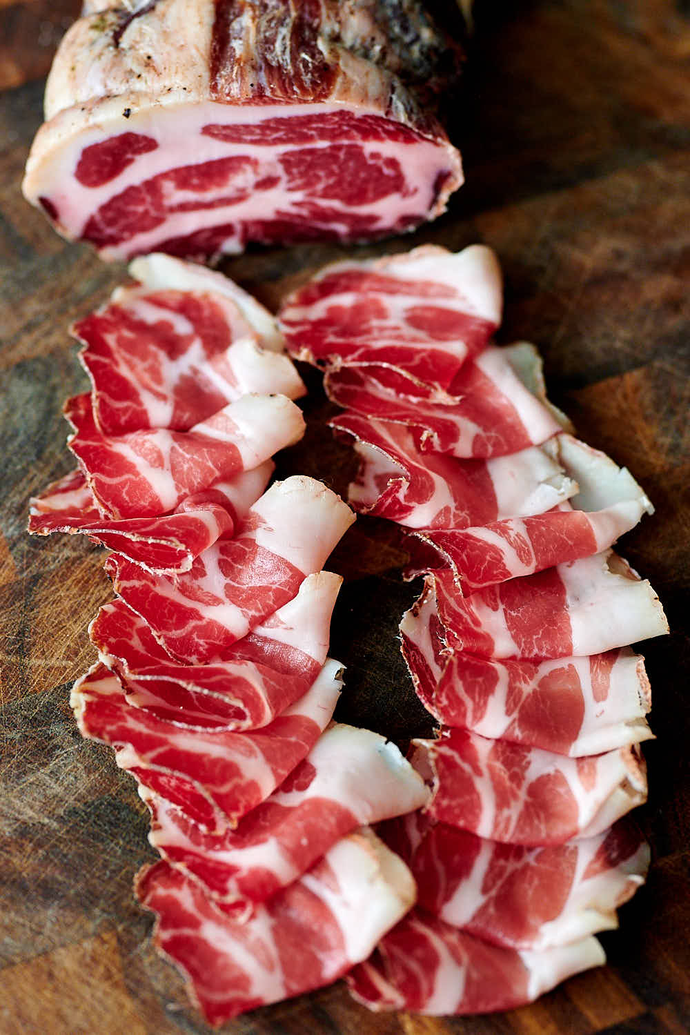 Sliced capicola on a wooden board.