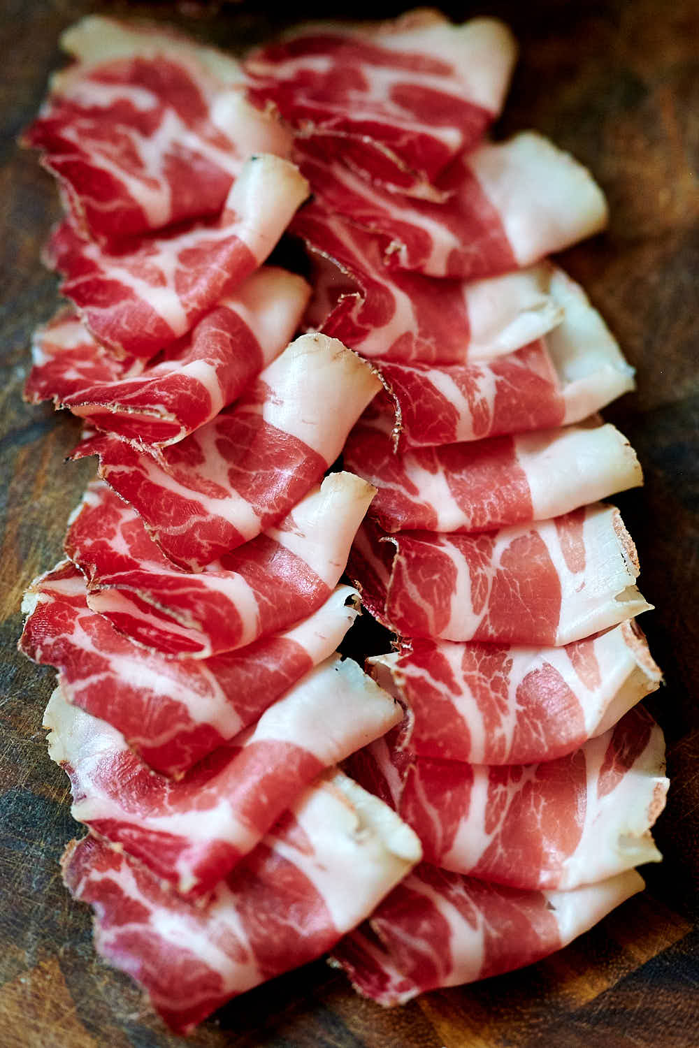 Thinly sliced capicola on a wooden board.