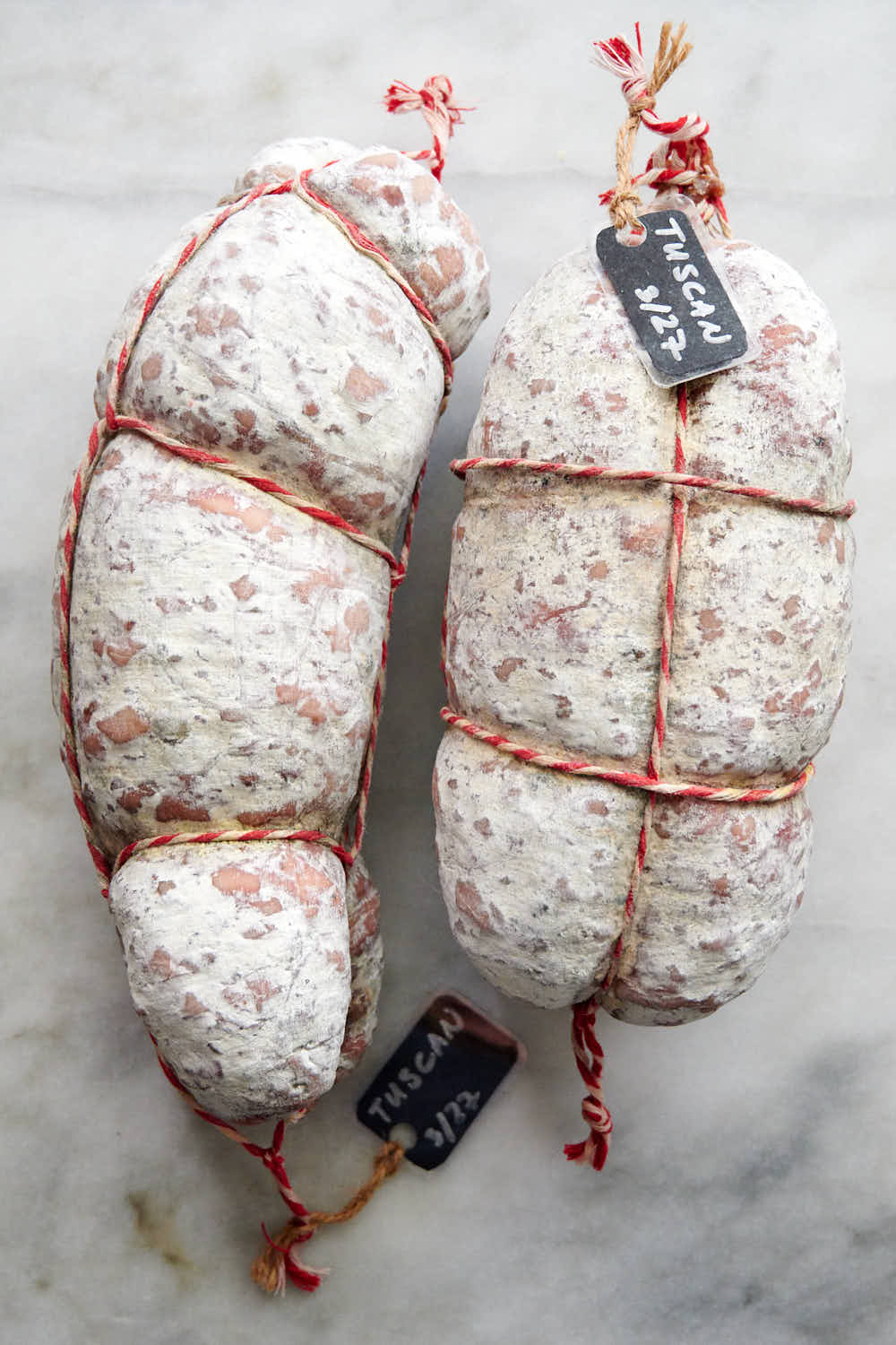Two Tuscan Salami tied with twine on a table.