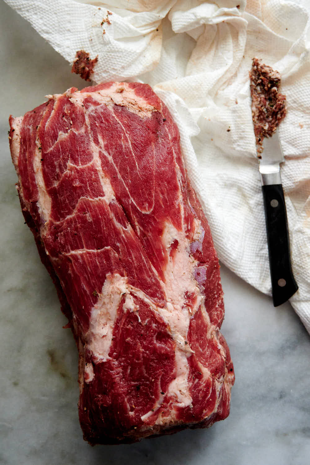 Scraping seasonings off cured capicola.