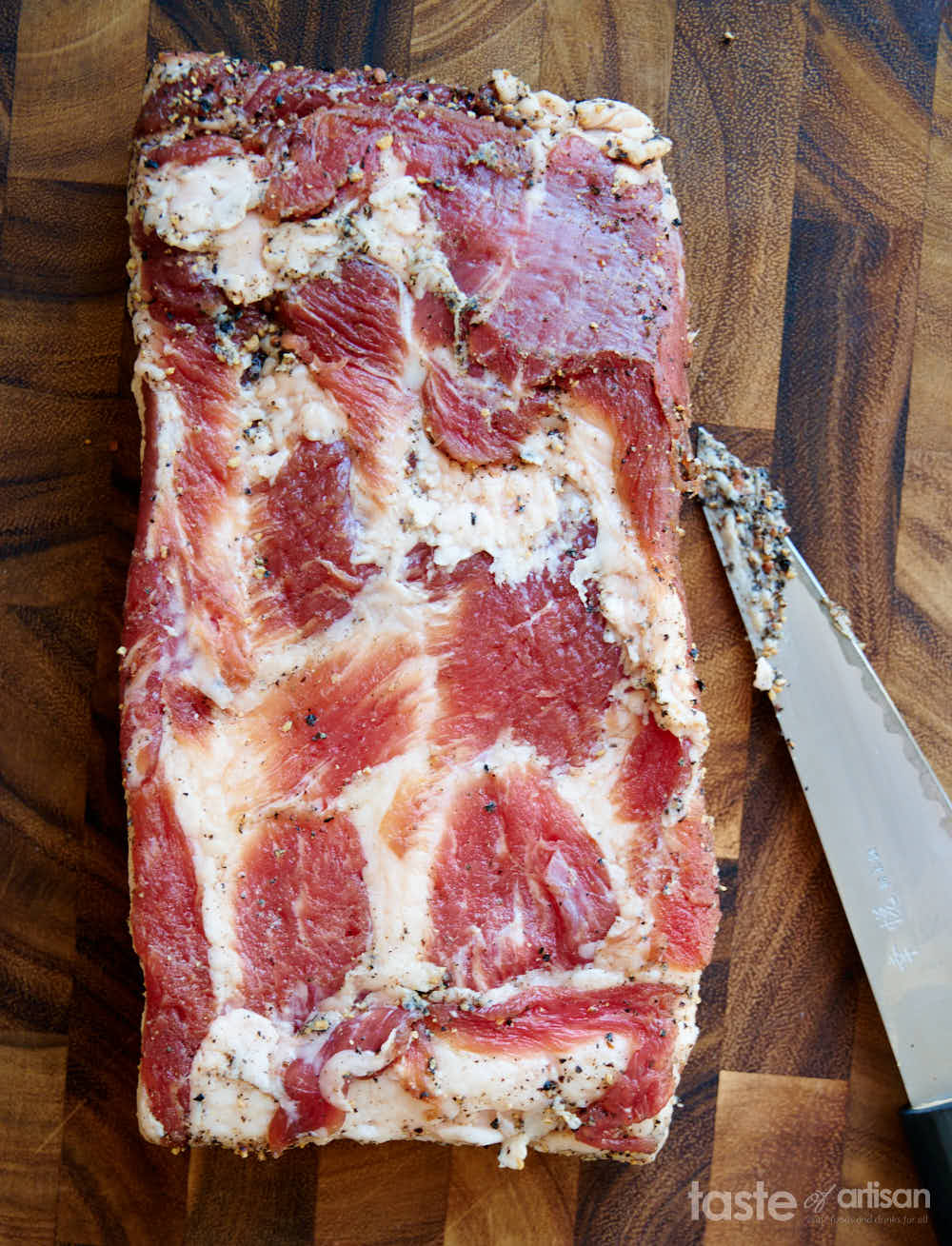 Scraping excess seasonings off cured bacon.