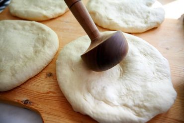 Pressing down center of dough for Uzbek bread obi non.