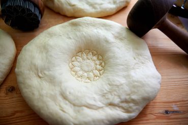 Stamps down center of dough with kechich for Uzbek bread obi non.