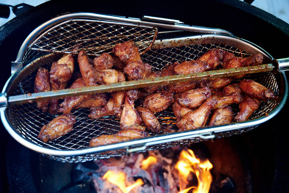 Chicken wings in rotisserie basket over hot charcoal.
