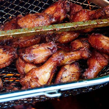 Rotisserie chicken wings in a basket over hot coals.