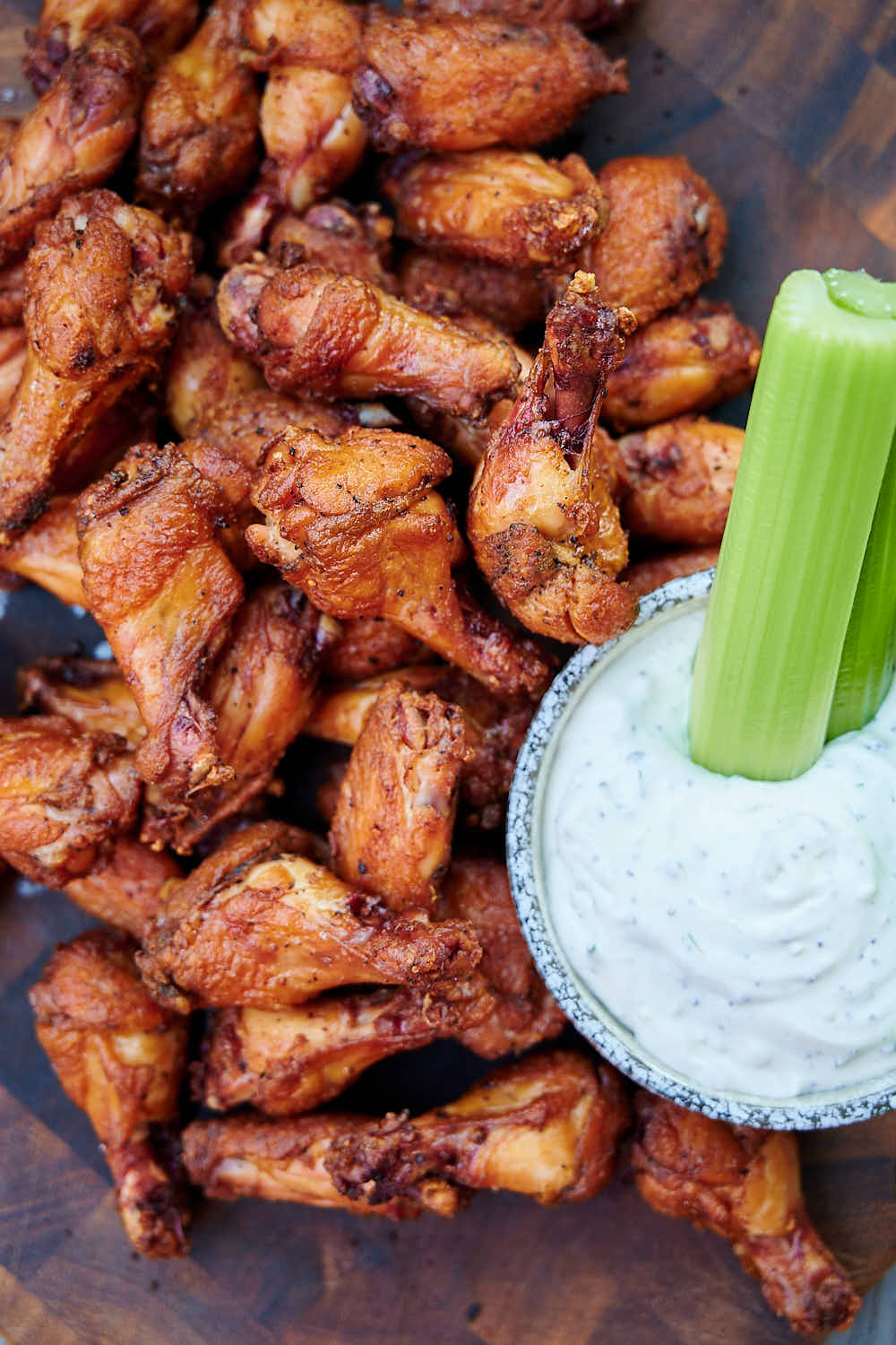Rotisserie chicken wings on a plate with dipping sauce and celery.