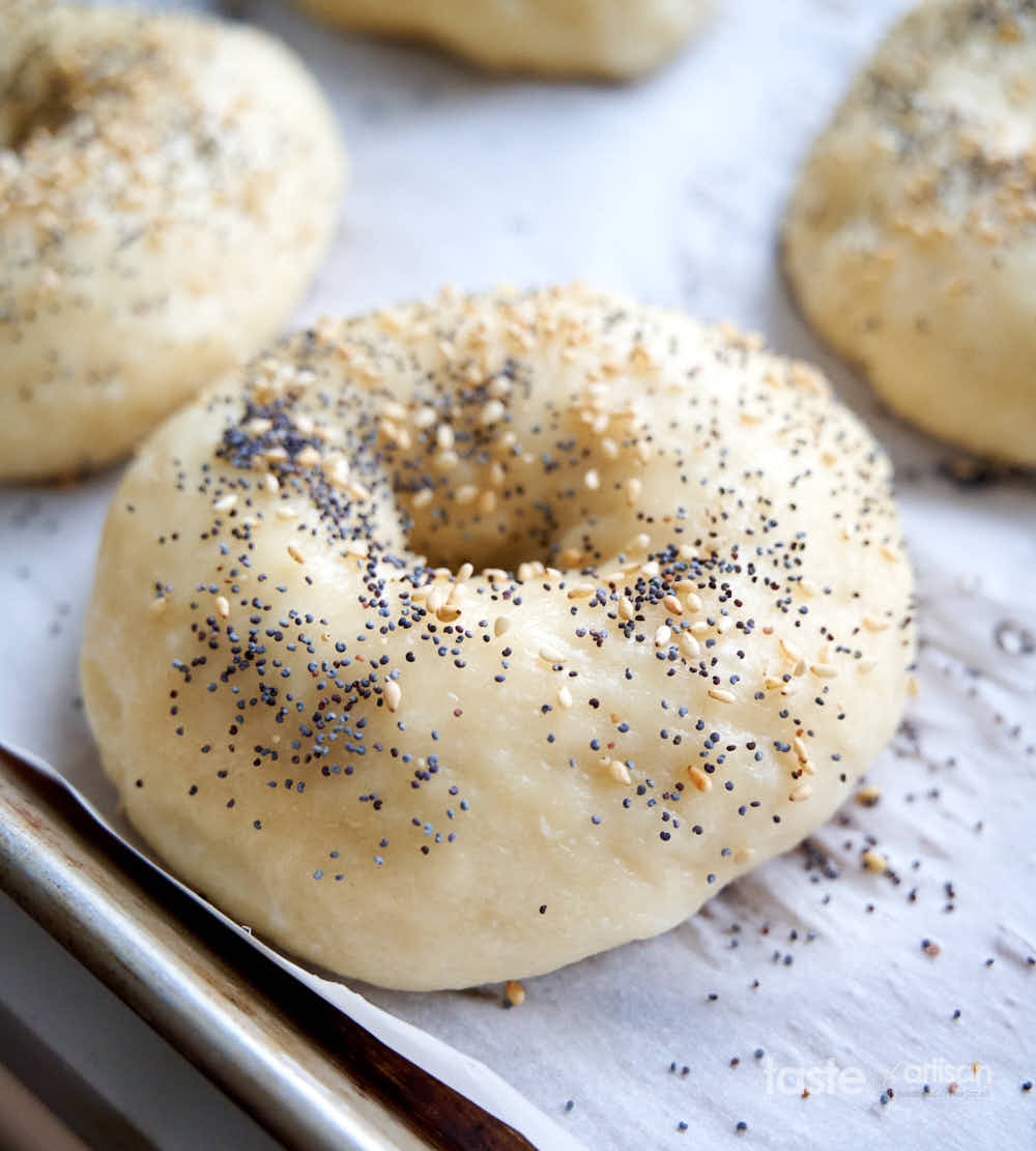 Boiled bagel dough rings sprinkled with poppy seeds and sesame seeds.