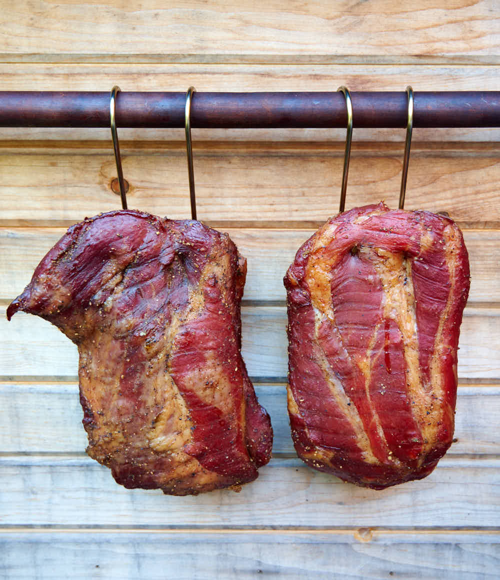 Buckboard bacon hanging outside smoker.