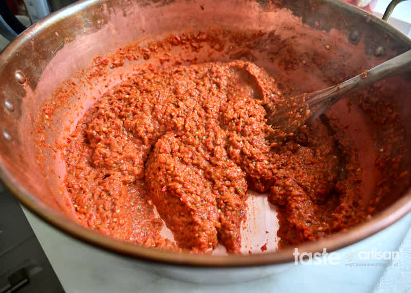 Ajvar, made according to a traditional ajvar recipe, cooking in a wide jam pan on a stove.