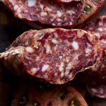 Spicy salami slices on a cutting board next to a spicy salami sandwich.