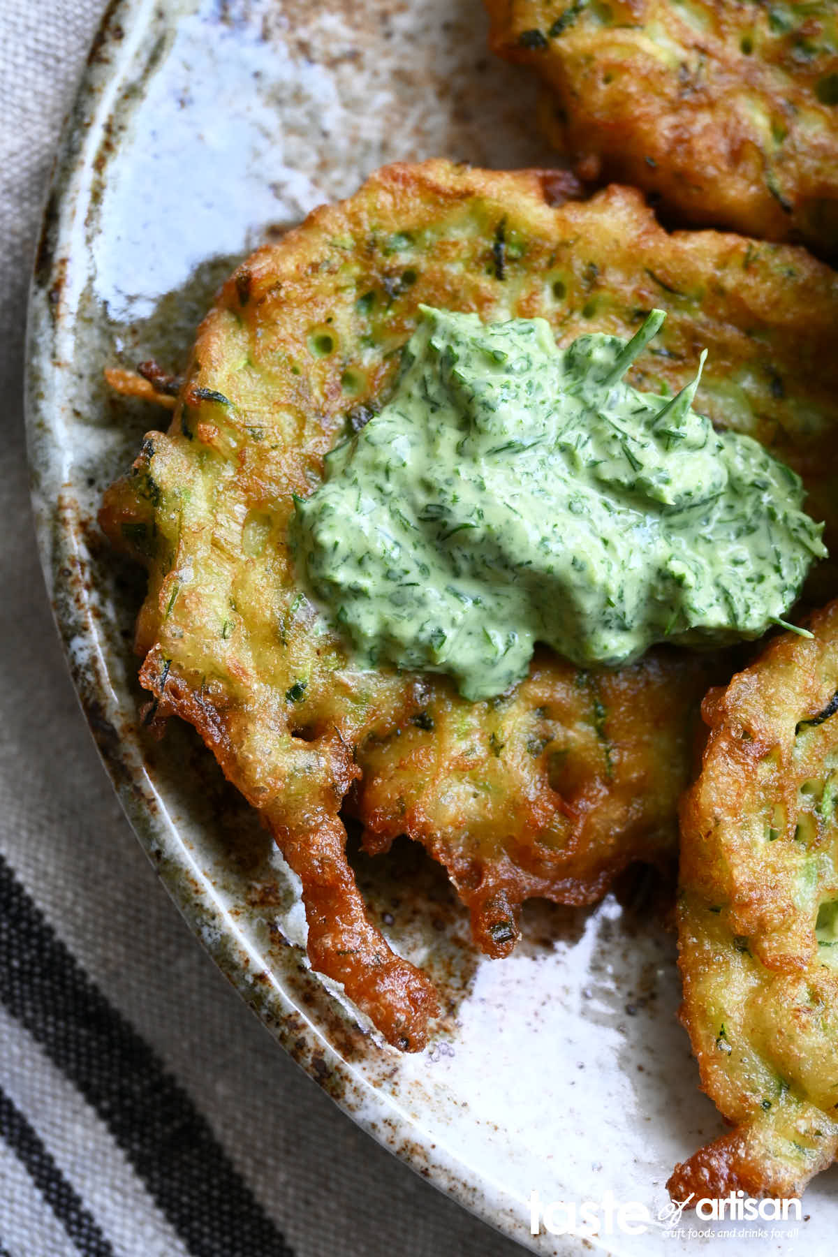 Zucchini pancakes on a plate with cilantro and mint sour cream dipping sauce.